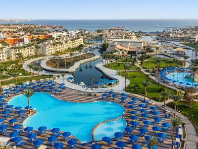 Vista aerea di un complesso alberghiero con grandi piscine, ombrelloni e vicino al mare.