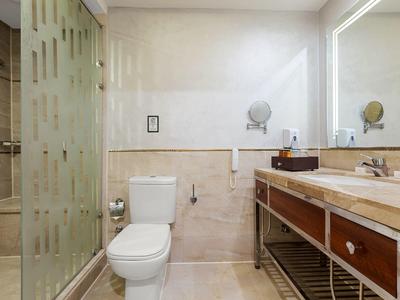 Helles Badezimmer mit Toilette, großer Waschtisch mit Spiegel und Dusche mit Glastür.