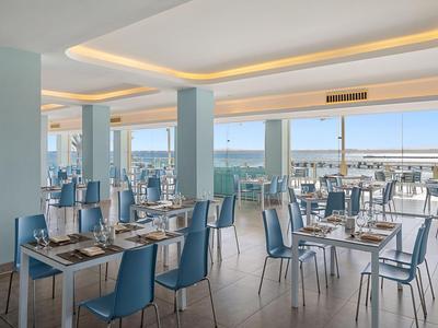 Restaurante moderno con sillas azules y vista al mar a través de grandes ventanas.