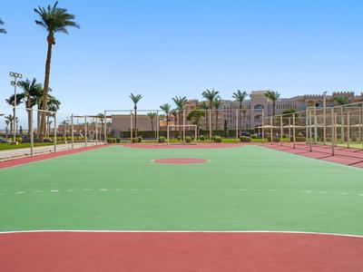 Leerer Tennisplatz mit roten und grünen Flächen, umgeben von Palmen und klarem blauem Himmel.