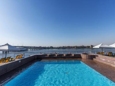 Hotelzwembad met uitzicht op een brede rivier onder een heldere blauwe lucht aan de oever.