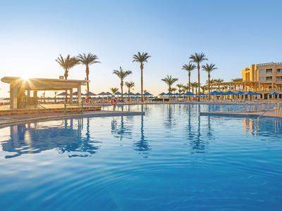 Grand piscine d'hôtel avec chaises longues, palmiers et eau calme au coucher du soleil.