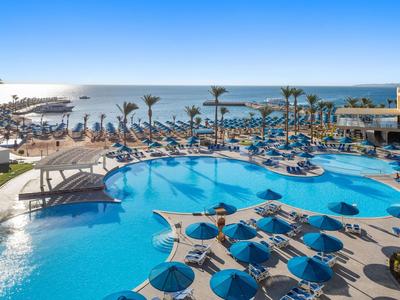 Grande piscine extérieure avec parasols bleus et vue sur la mer sous un ciel clair.