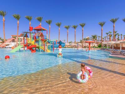 Des enfants jouent dans une piscine peu profonde avec des toboggans colorés et des palmiers en arrière-plan.