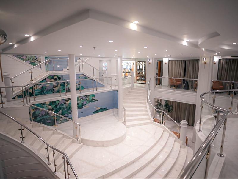 Weißer, moderner Innenraum mit geschwungenen Treppen, Glasgeländern und großen Fenstern.