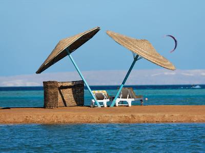 Dos tumbonas con sombrillas de paja en una playa junto al mar azul bajo un cielo despejado.