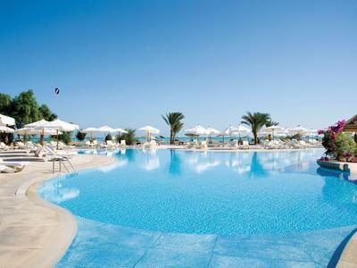 Large hotel pool with sun umbrellas and palm trees under a clear sky