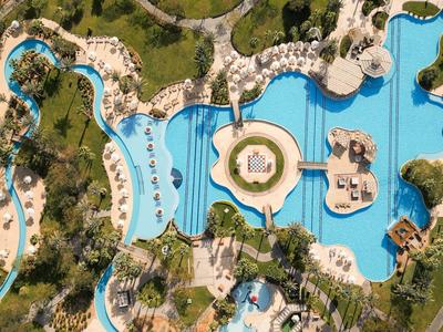 Vue aérienne d'une grande piscine d'hôtel sinueuse avec des palmiers et des chaises longues