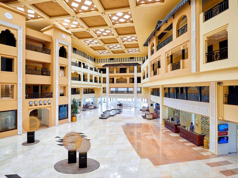 Ruim, licht hotelatrium met marmeren vloer, vier verdiepingen en moderne zithoeken.