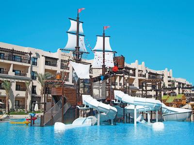 Glijbanen en een piratenschip-speelplaats voor een hotel onder een blauwe lucht.