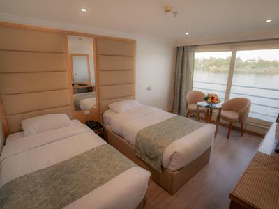 Zweibettzimmer mit Holzdekor, großen Fenstern und Blick auf einen Fluss, zwei Stühle, Nachttisch.