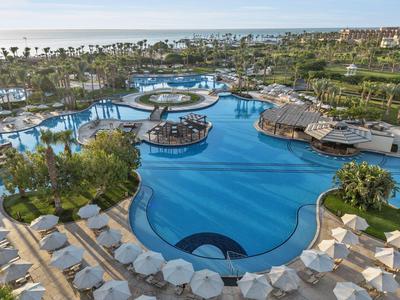 Großer Hotelpool mit Sonnenschirmen, Liegestühlen und Poolbars in tropischer Umgebung.