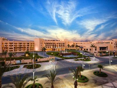 Gran edificio de hotel al atardecer con caminos iluminados y palmeras.