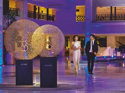 Coppia in abiti eleganti che cammina in un cortile illuminato e moderno con decorazioni contemporanee.