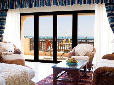 Bright living room with armchairs, table, and large window overlooking terrace and sea.