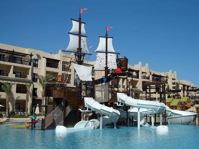 A large pool with a pirate ship-themed water slide in front of a hotel
