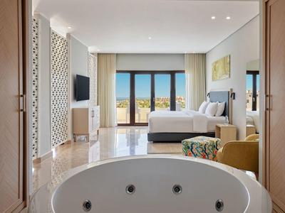 Modern hotel room with open whirlpool, large bed, and big window overlooking the city.