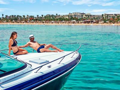 Una coppia si rilassa su una barca in acqua turchese limpida vicino alla costa con spiaggia e hotel.