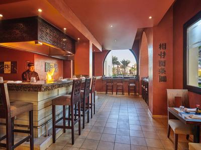 Przytulny bar hotelowy z wysokimi krzesłami i dużym oknem z widokiem na miasto.