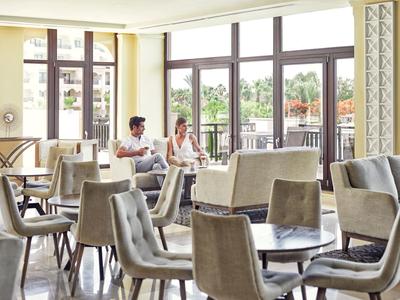 Restaurante moderno y luminoso con grandes ventanales y sillas tapizadas grises, dos huéspedes conversando.