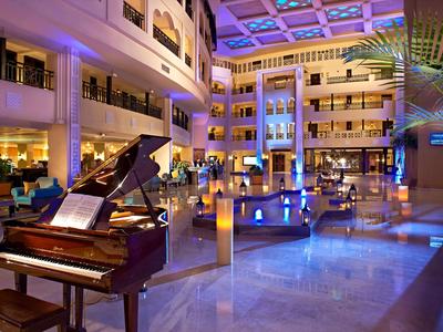 Ruime hotel lobby met vleugelpiano, moderne zithoeken en sfeerverlichting.