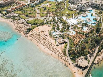 Resort sulla spiaggia con acqua limpida, lettini e piscina immersi nel verde.