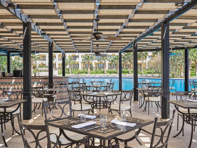 Terrasse extérieure couverte avec tables donnant sur une piscine dans un complexe.