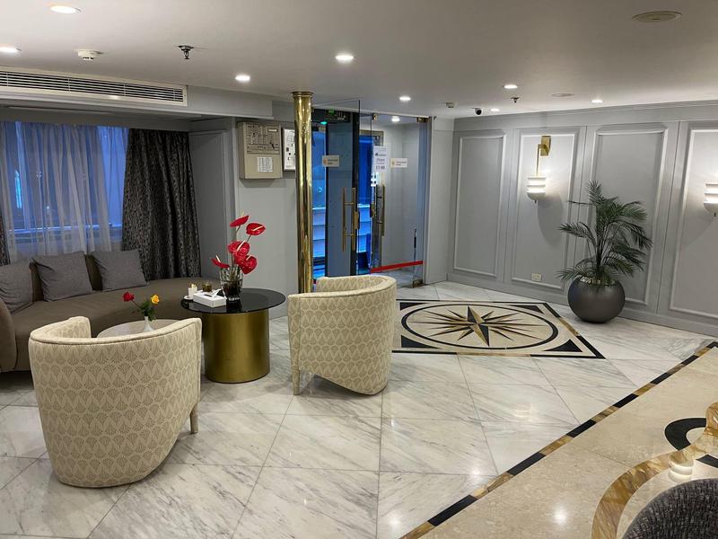 Elegantní hotelový salon s křesly, pohovkou, rostlinou a kobercem s geometrickým vzorem.