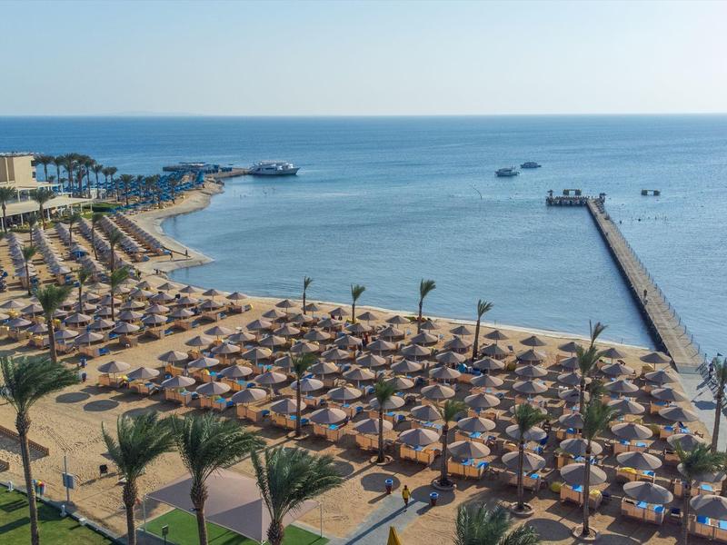 Strandresort mit Liegestühlen, Sonnenschirmen und einer langen Pier am Meer.