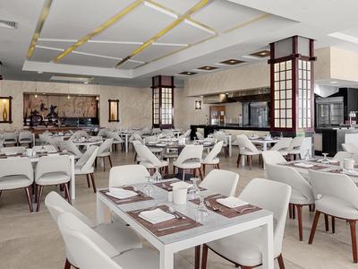 A modern, bright restaurant with white chairs and set tables in a hotel.