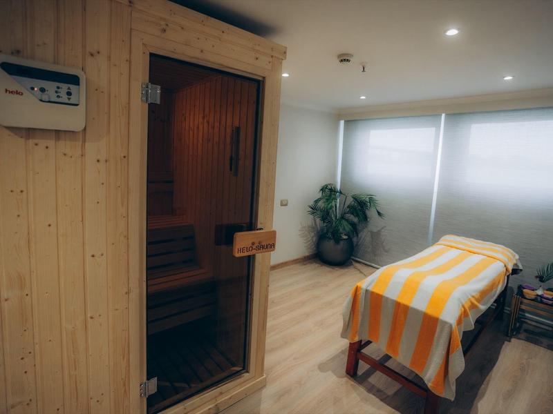 Sala massaggi luminosa con tavolo e sauna in legno.