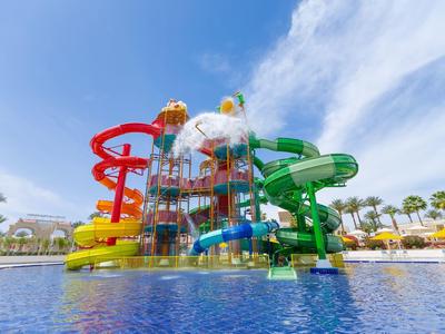 Parque acuático colorido con toboganes y juegos de agua bajo cielo despejado y palmeras.