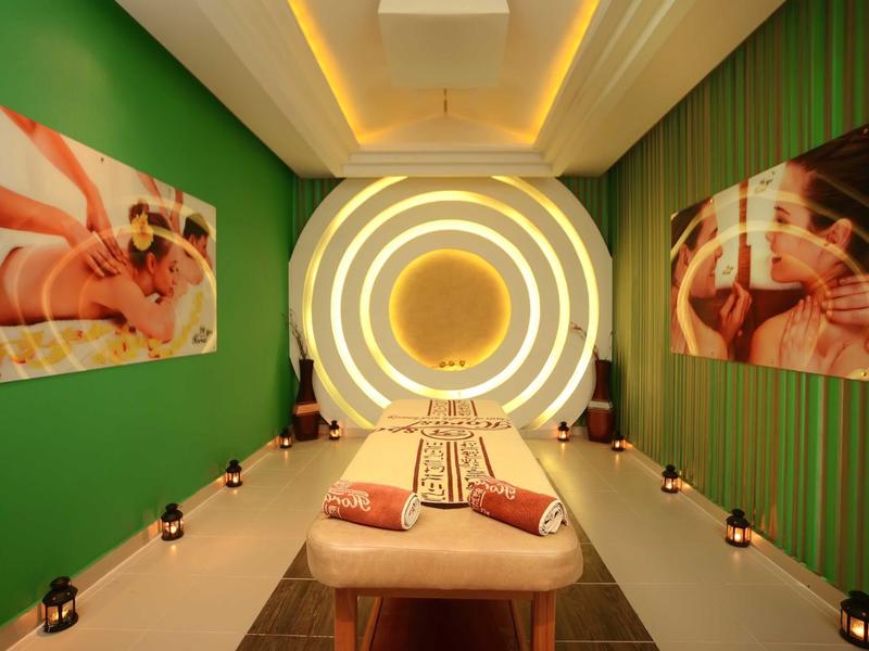 Sala de masajes con paredes verdes, iluminación circular cálida y camilla con cojines.