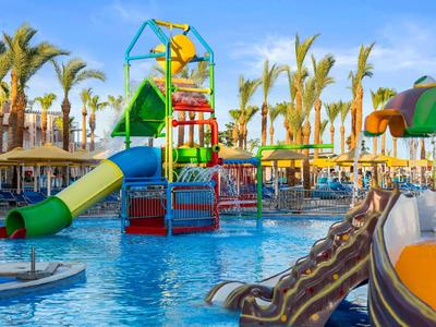 Kleurrijk waterspeelgebied met glijbanen en palmbomen in een hotelzwembad bij zonnig weer.