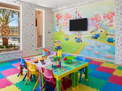 Bunter Kinderspielraum mit Spieltisch, kleinen Stühlen und cartoonhaften Wandbildern.