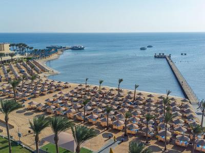 Plage avec parasols, chaises longues, palmiers et une jetée s'étendant dans la mer.