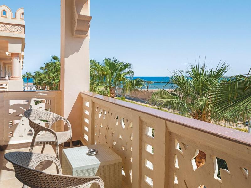 Balcon avec chaises et vue sur la mer et des palmiers par une journée ensoleillée.