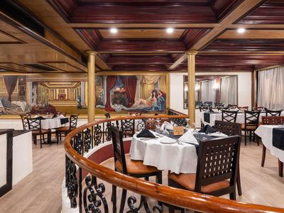 Ristorante elegante con tavoli apparecchiati e murales alle pareti in luce calda.