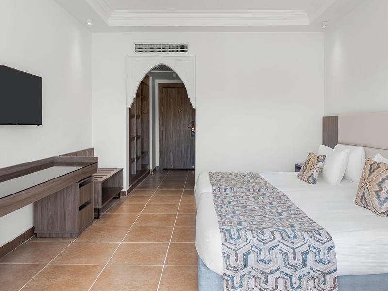 Modern hotel room with double bed, flat-screen TV, wooden furniture, and bright walls.