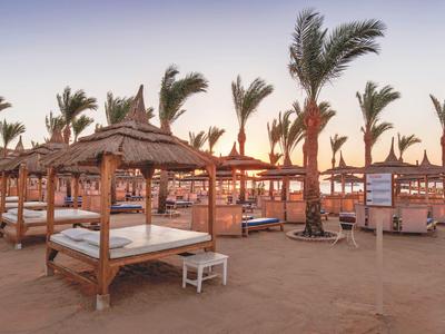 Playa con camas de sombra de palma y tumbonas al atardecer en un resort hotelero.