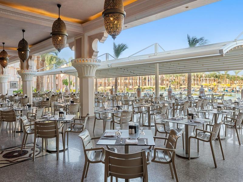 Gran terraza abierta de hotel con muchas mesas y sillas, lámparas decorativas y vista al mar.