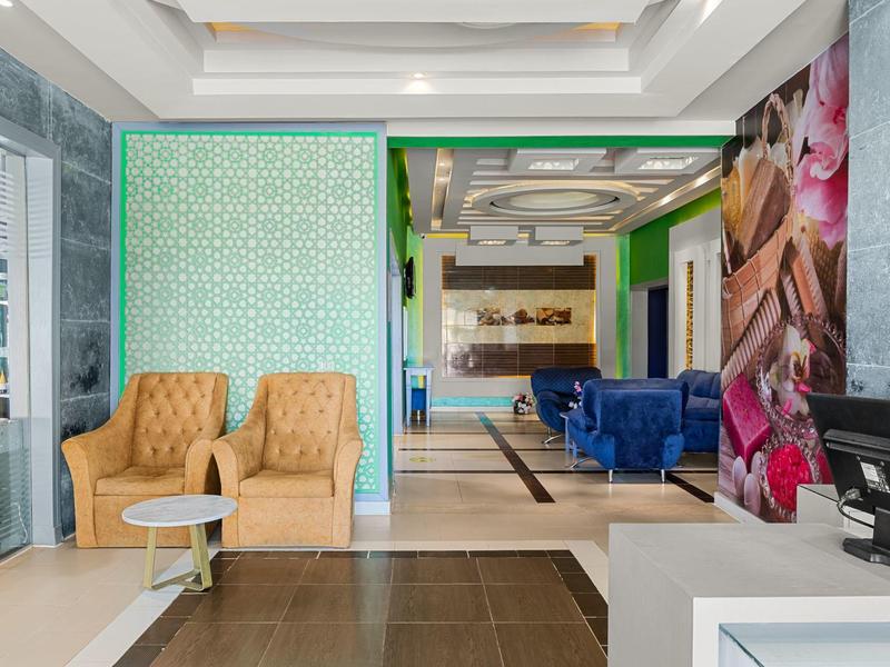 Moderna recepción de hotel con sillones beige, mesa blanca, área de asientos azul y decoración mural.