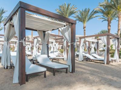 Mehrere Strandpavillons mit weißen Vorhängen und Liegestühlen unter Palmen auf Sand.