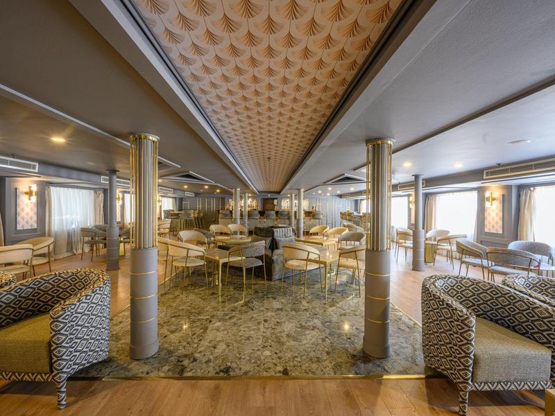 Spacious lounge area with modern chairs, marble floor, columns, and large windows for natural light.