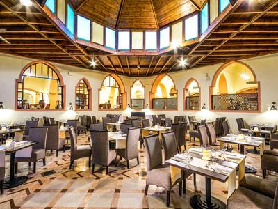 Przestronna restauracja hotelowa z drewnianym sufitem, okrągłymi oknami i elegancko nakrytymi stolikami.