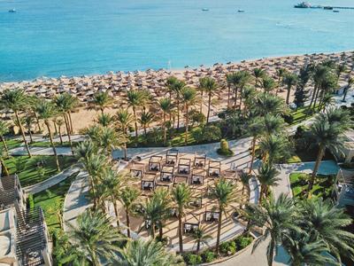 Strandhotel met palmbomen, parasols en uitzicht op de blauwe zee op de achtergrond.