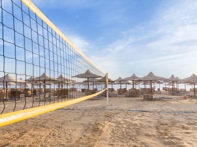 Leerer Sandstrand mit Volleyballnetz und Reihen von Strohhütten unter blauem Himmel.