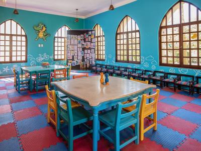 Sala colorata con tavoli quadrati, sedie multicolori e grandi finestre ad arco.