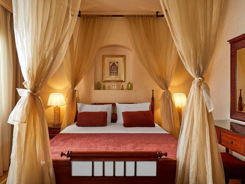 Camera elegante con letto a baldacchino, tende trasparenti e illuminazione calda.