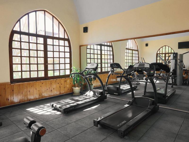 Hotel gym with treadmills, large arched windows, mirrored wall, and wooden paneling.